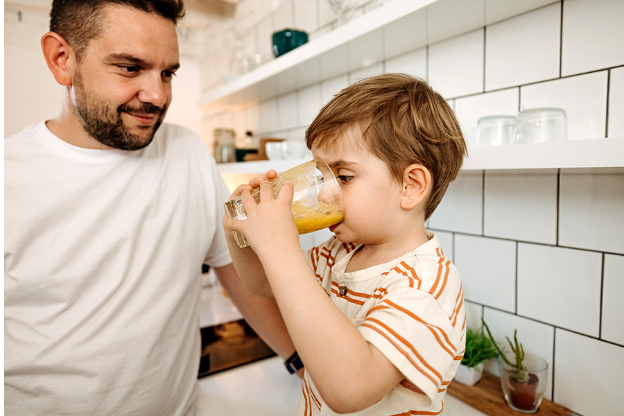 Child drinking juice while adult watches nearby.
