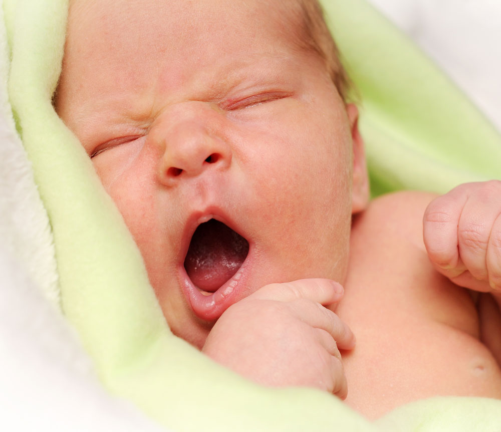 Newborn baby yawning wrapped in green blanket