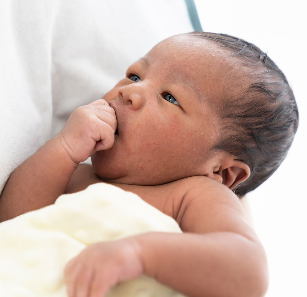 Newborn sucking hand, resting on shoulder