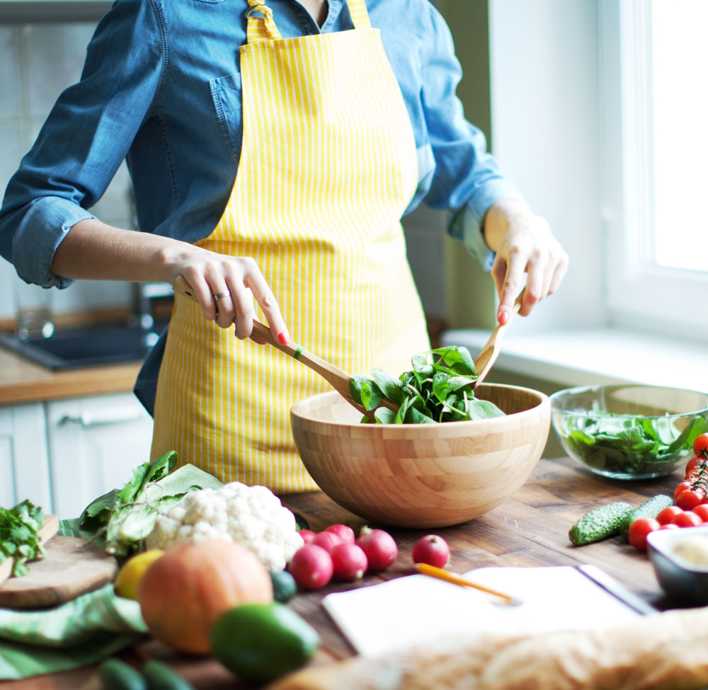 Woman tossing fresh salad in wooden bowl