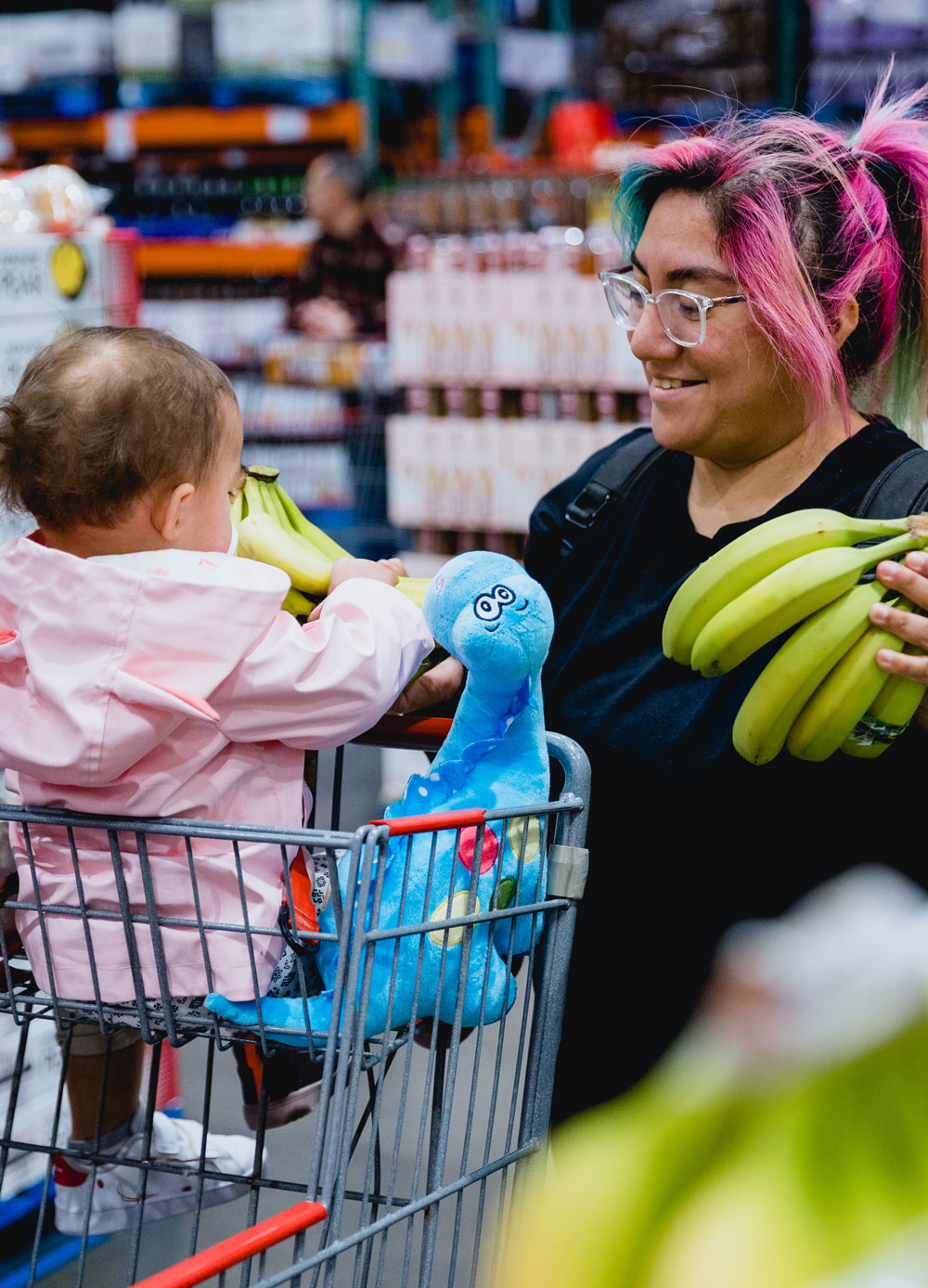 smiles at a baby in a shopping cart, both holding bananas