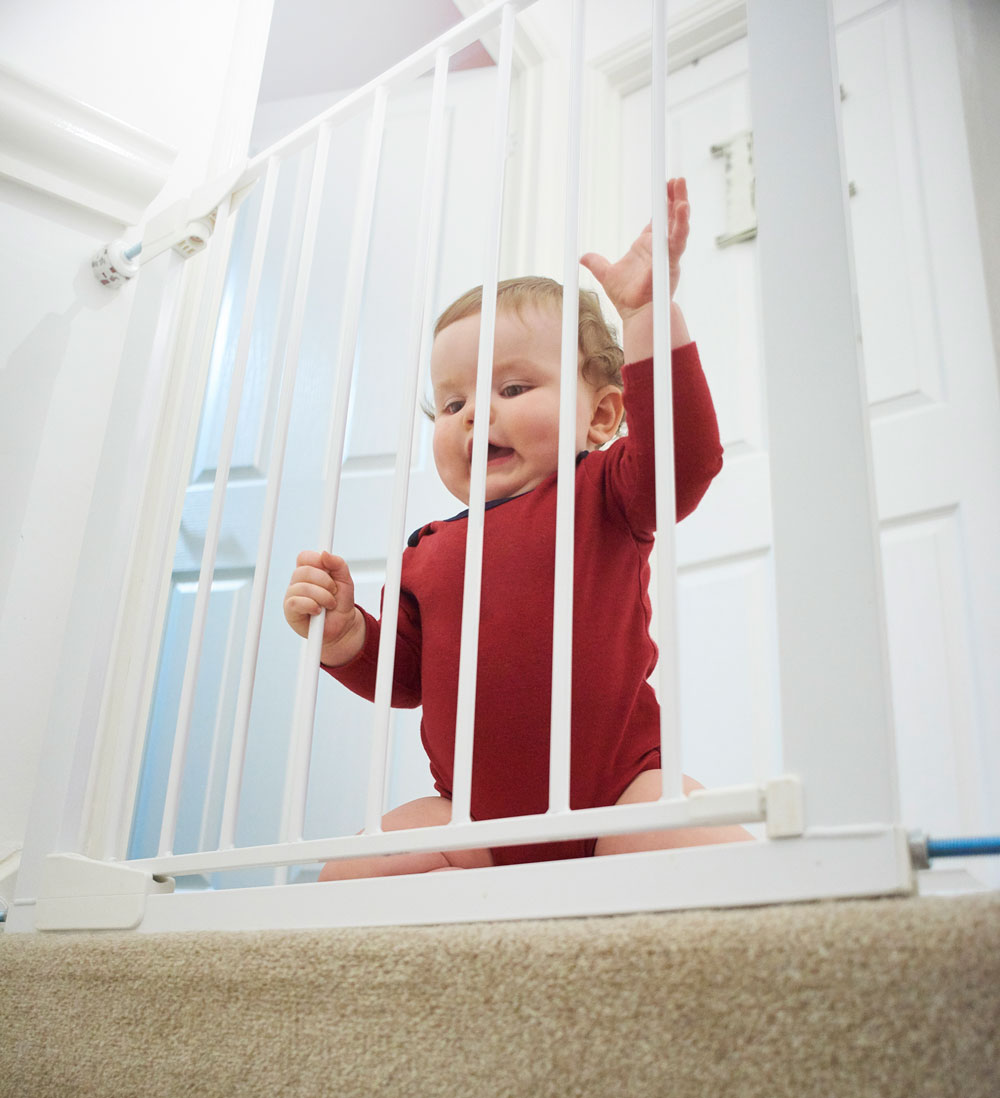 Baby standing behind white safety gate at stairs