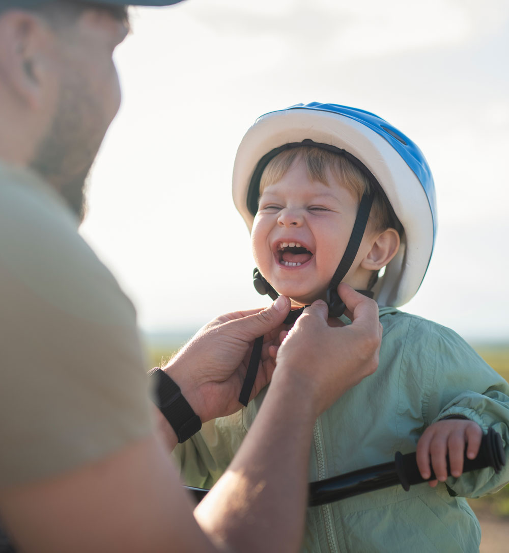 Father fastening bike helmet on laughing toddler
