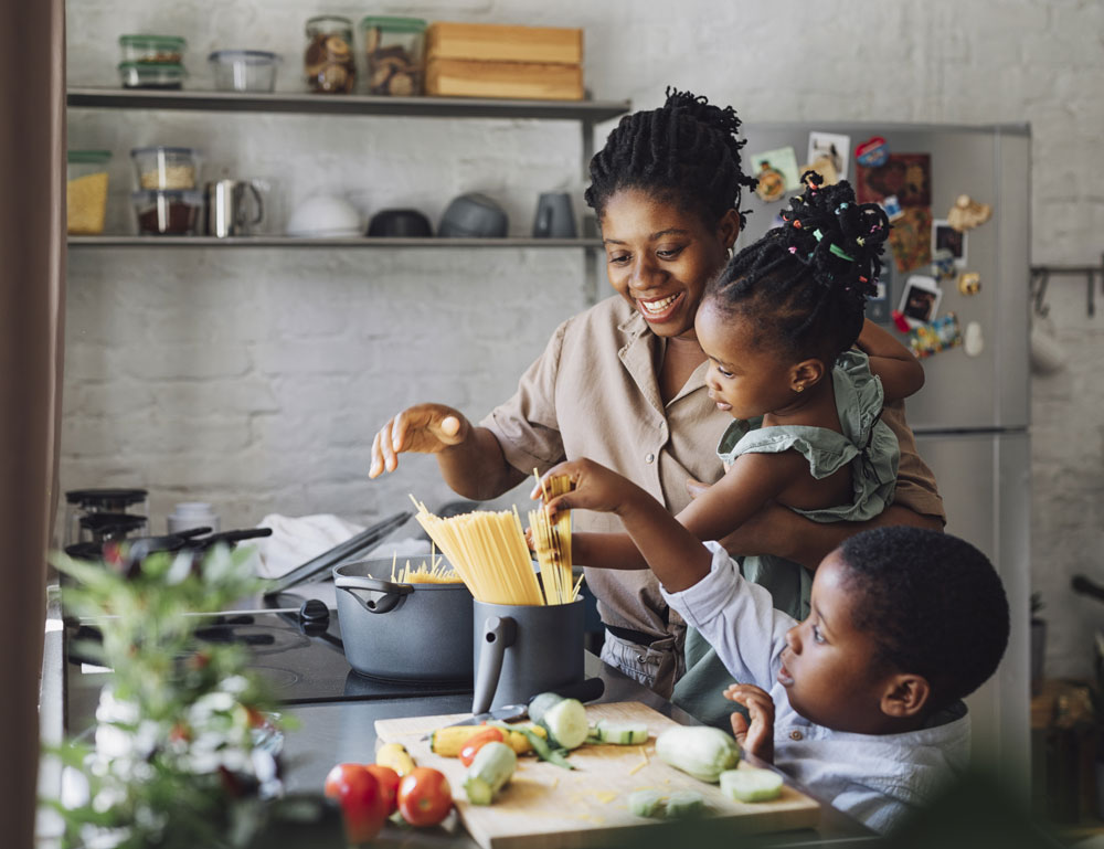 Mother cooking pasta with two children in kitchen