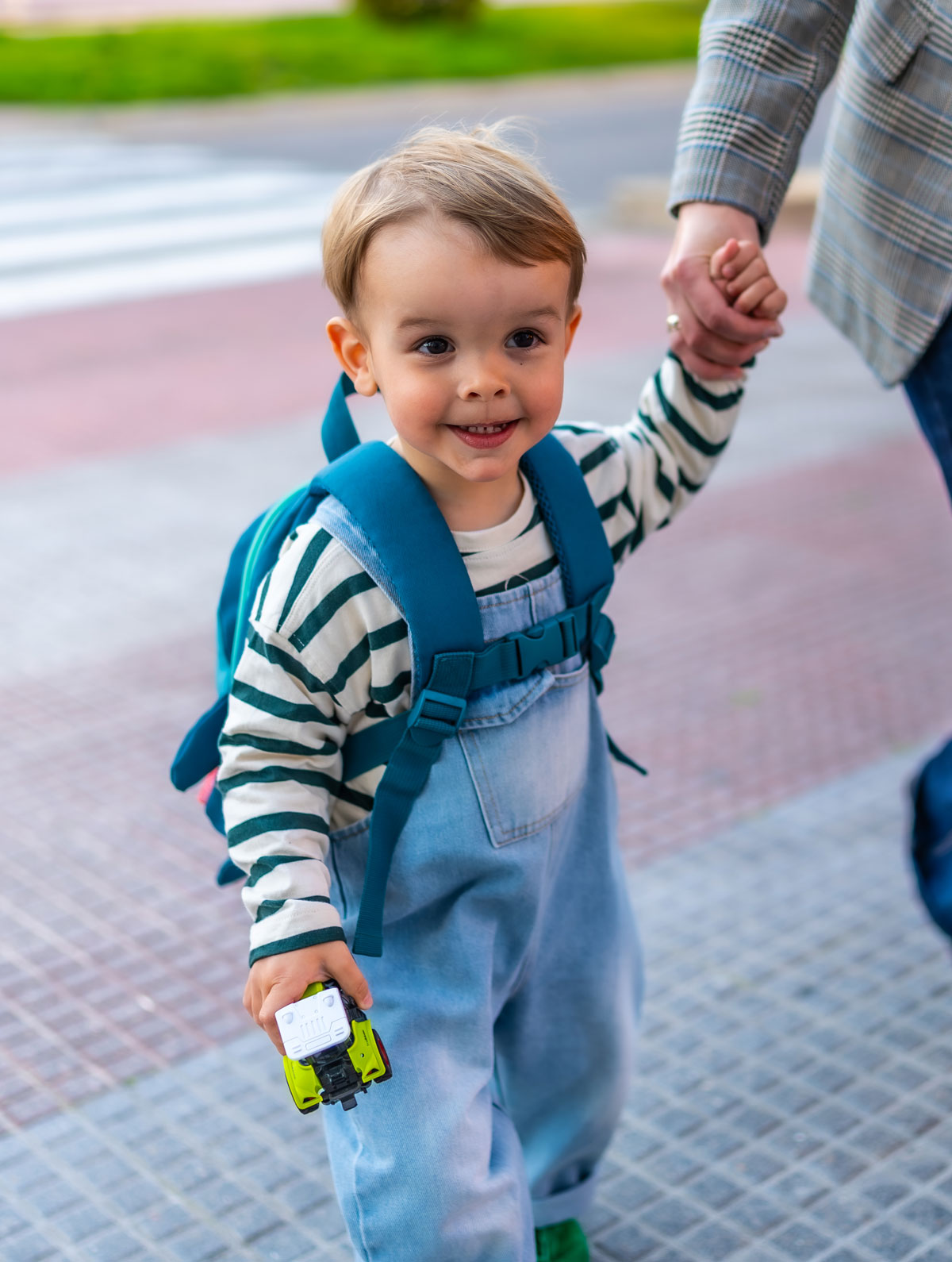 Toddler holding parents hand, walking outdoors smiling