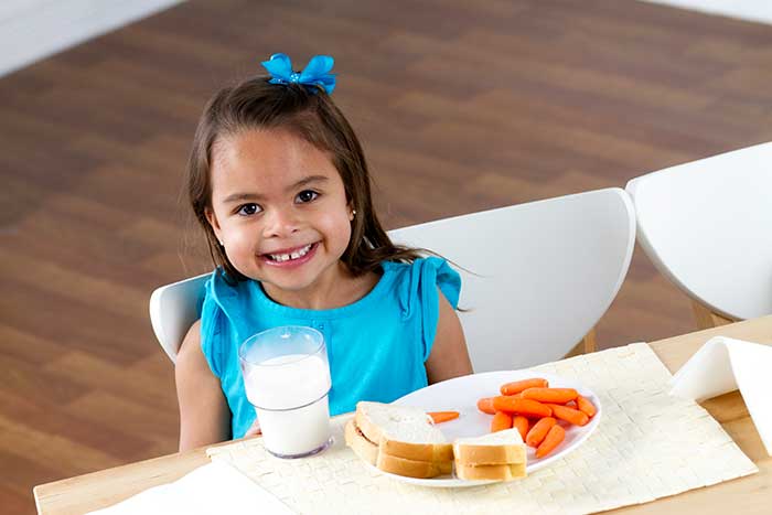 Smiling girl enjoying meal with milk and carrots.