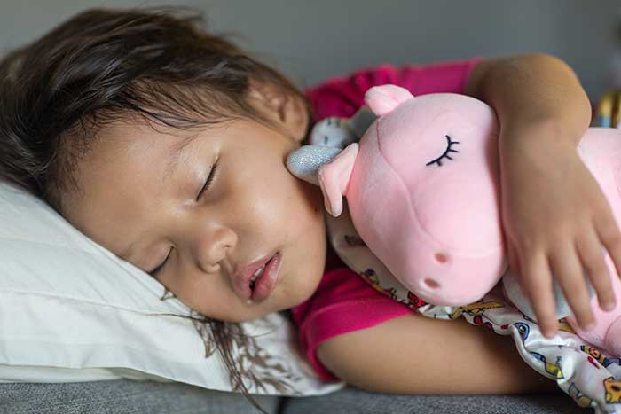 Child sleeping, hugging pink plush unicorn tightly.