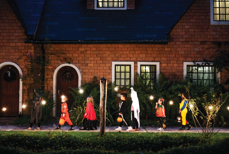 Children trick-or-treating in costumes outside charming house.